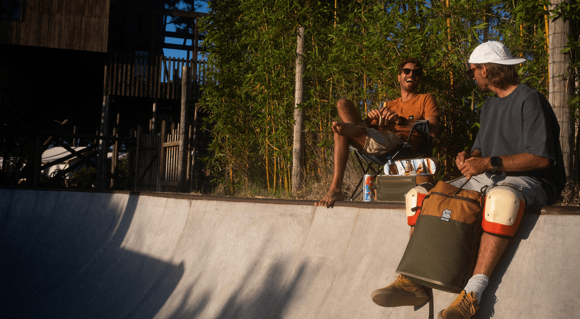 Two skateboarders sitting on a concrete ledge with skateboards, surrounded by greenery.